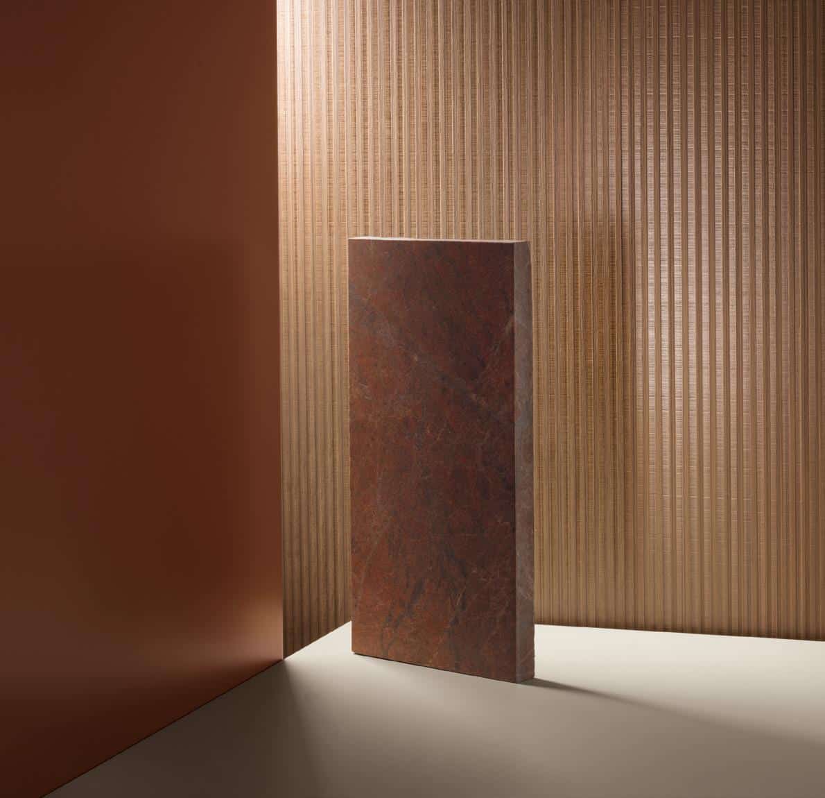 A vertical slab of dark brown marble leaning against a textured beige wall with subtle lighting.