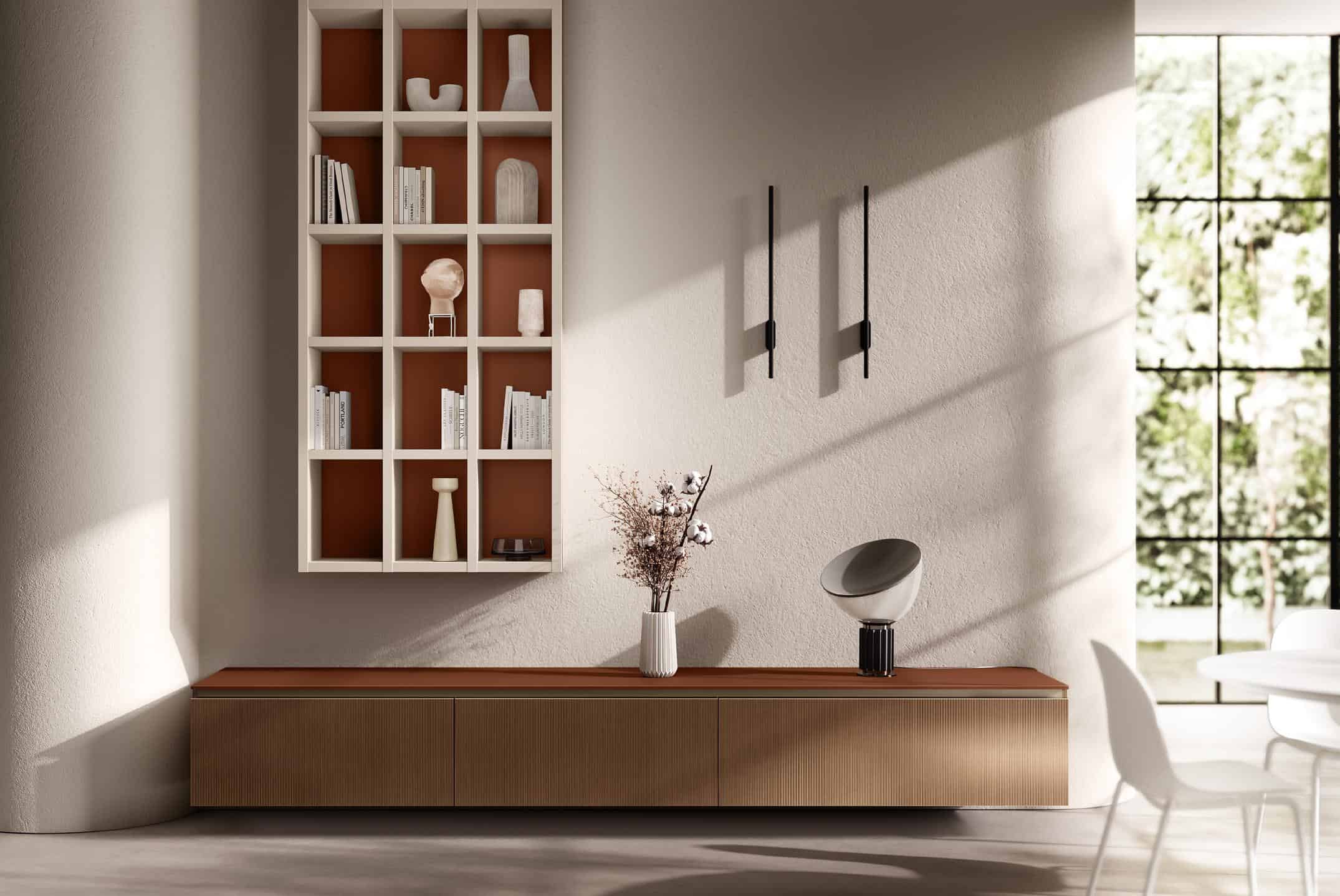 A modern living room with a wooden console, wall-mounted shelves displaying books and decorative objects, two vertical wall sconces, and a vase with branches. Large windows and minimalist furniture complete the space.