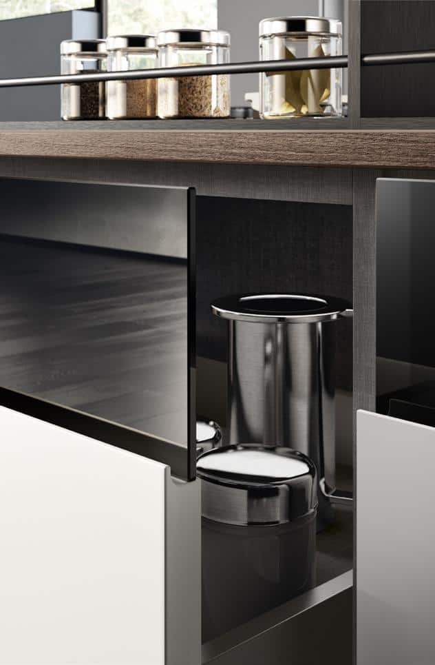Modern kitchen cabinet with open door, revealing stainless steel containers inside. Multiple glass jars with various dry food items on the wooden countertop above.
