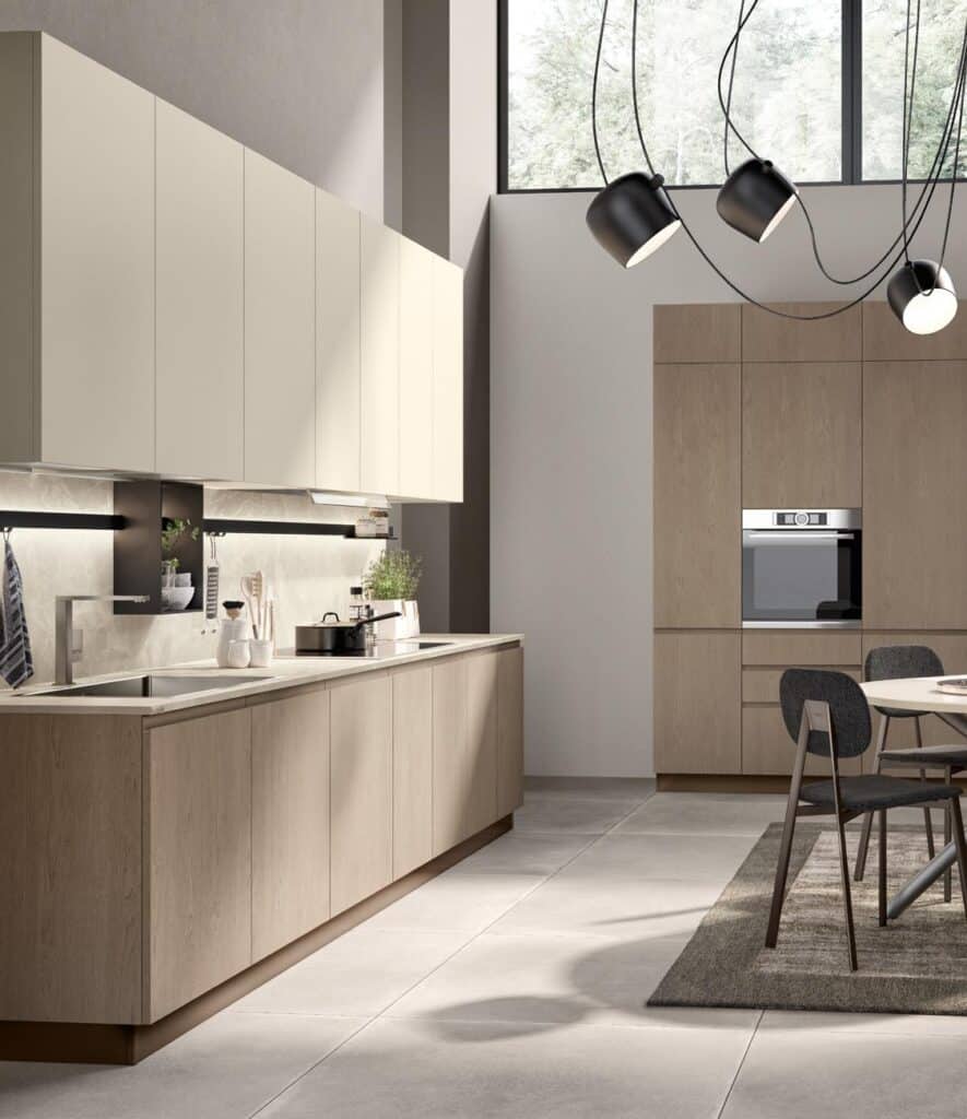 Modern kitchen with light wood cabinetry, beige wall units, built-in oven, large window, and contemporary lighting.