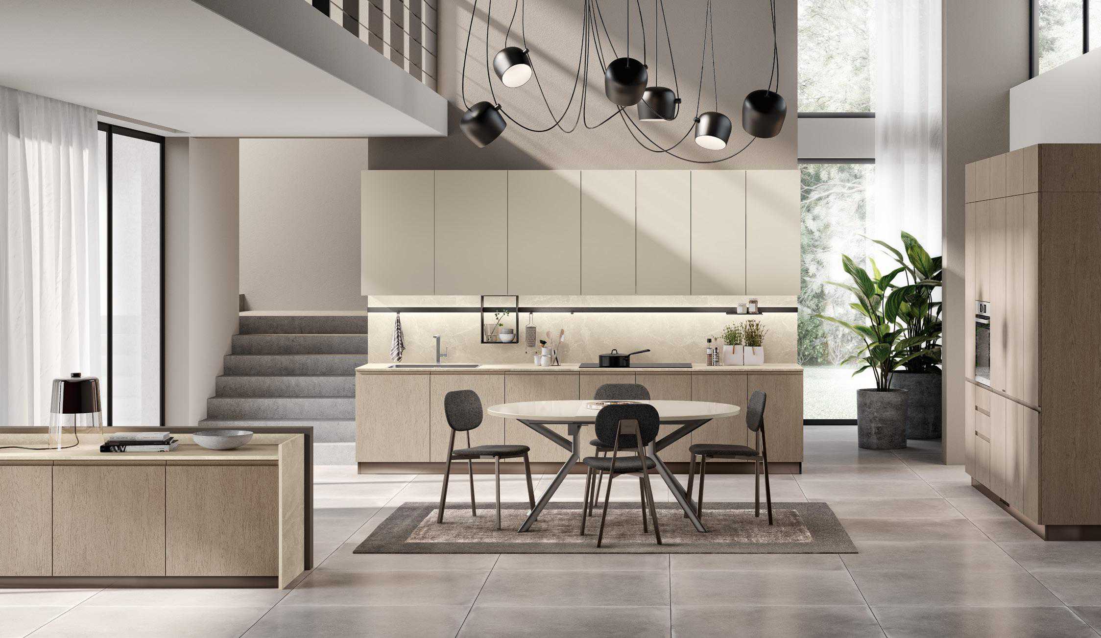 Modern kitchen and dining area with beige cabinets, a round dining table with four chairs, large windows, staircase, and ceiling lights.