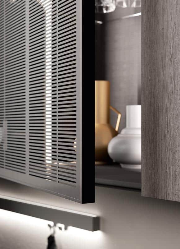A close-up of a kitchen cabinet with a partially open door featuring a slatted design, revealing vases and jars inside.