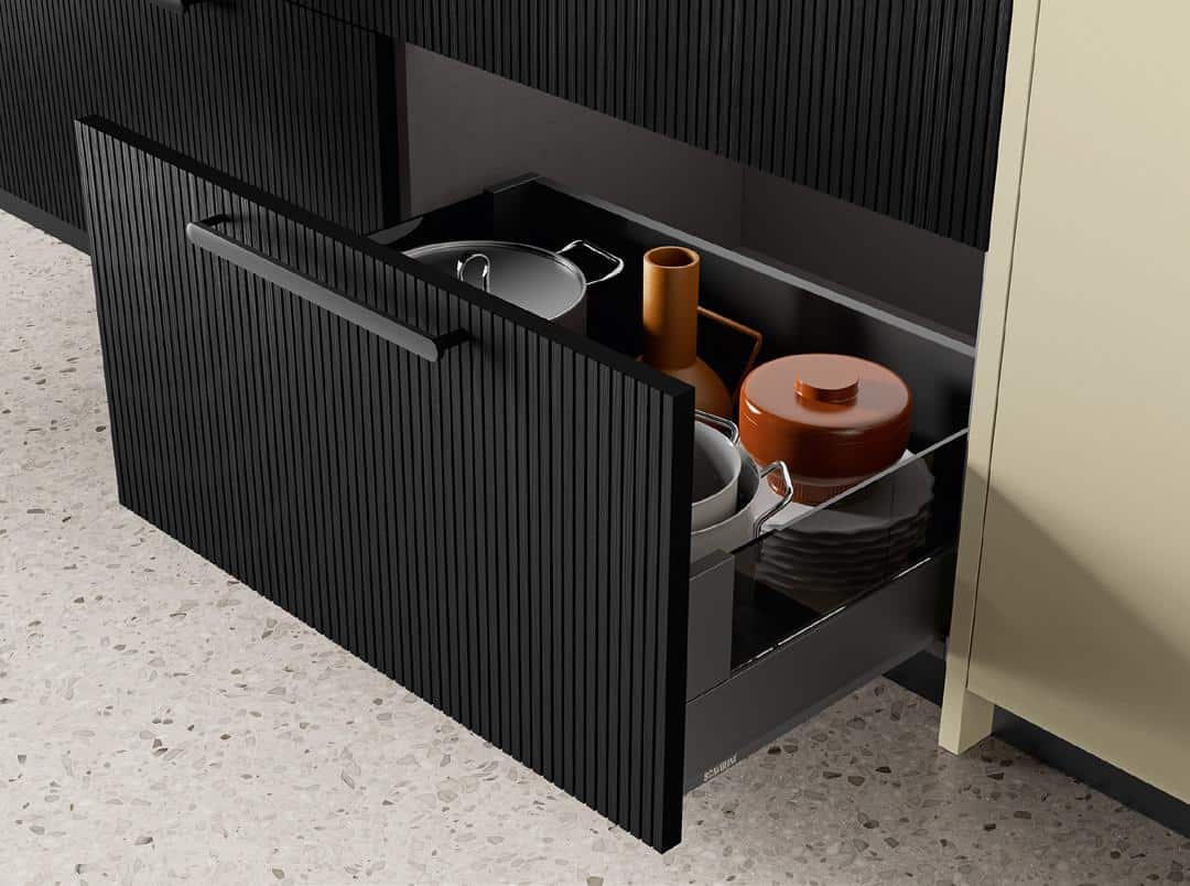 Open kitchen drawer with pots, bowls, and vases inside against a speckled floor.