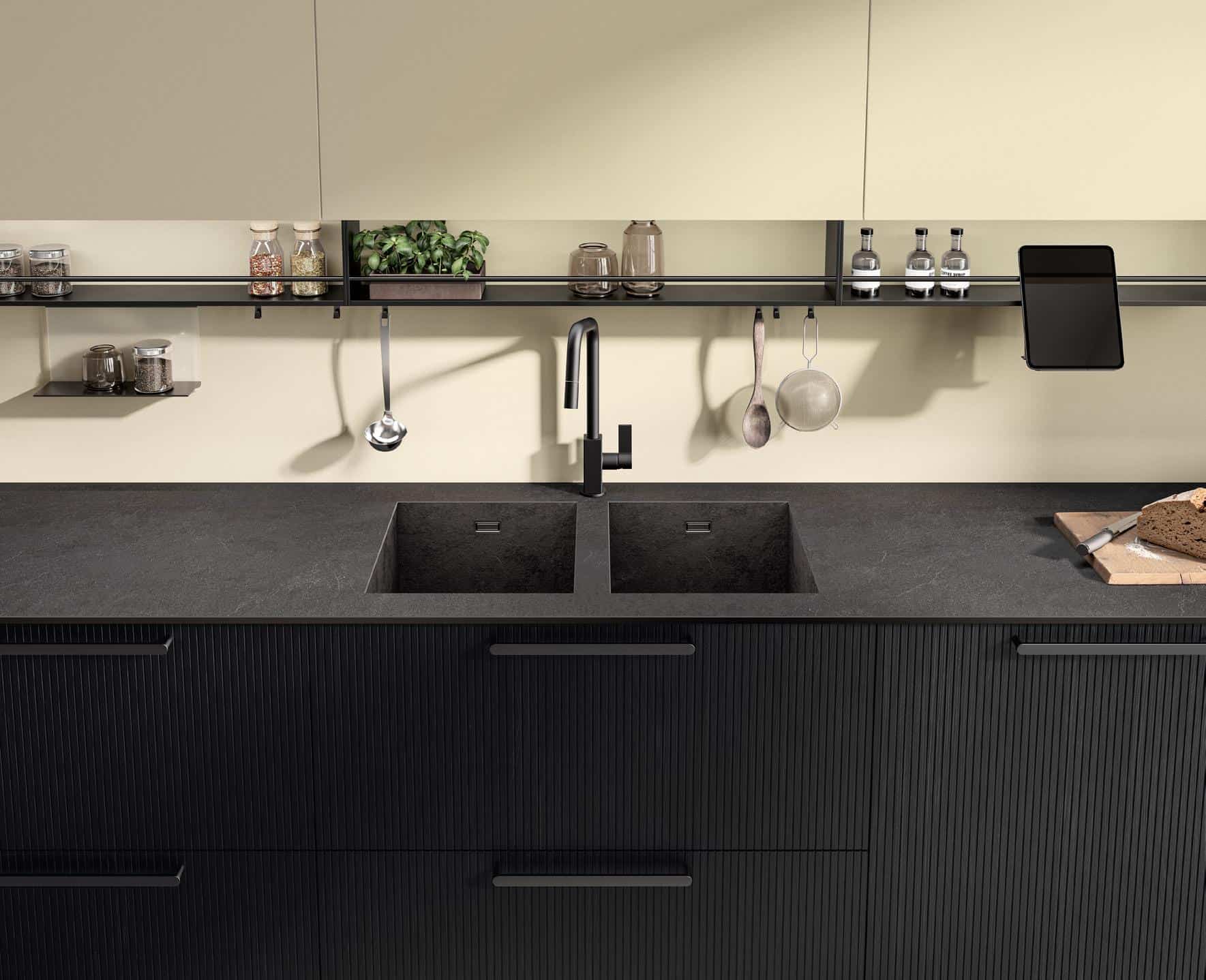 Modern kitchen with black double sink, sleek faucet, dark countertop, hanging utensils, and floating shelves with spices and plants.