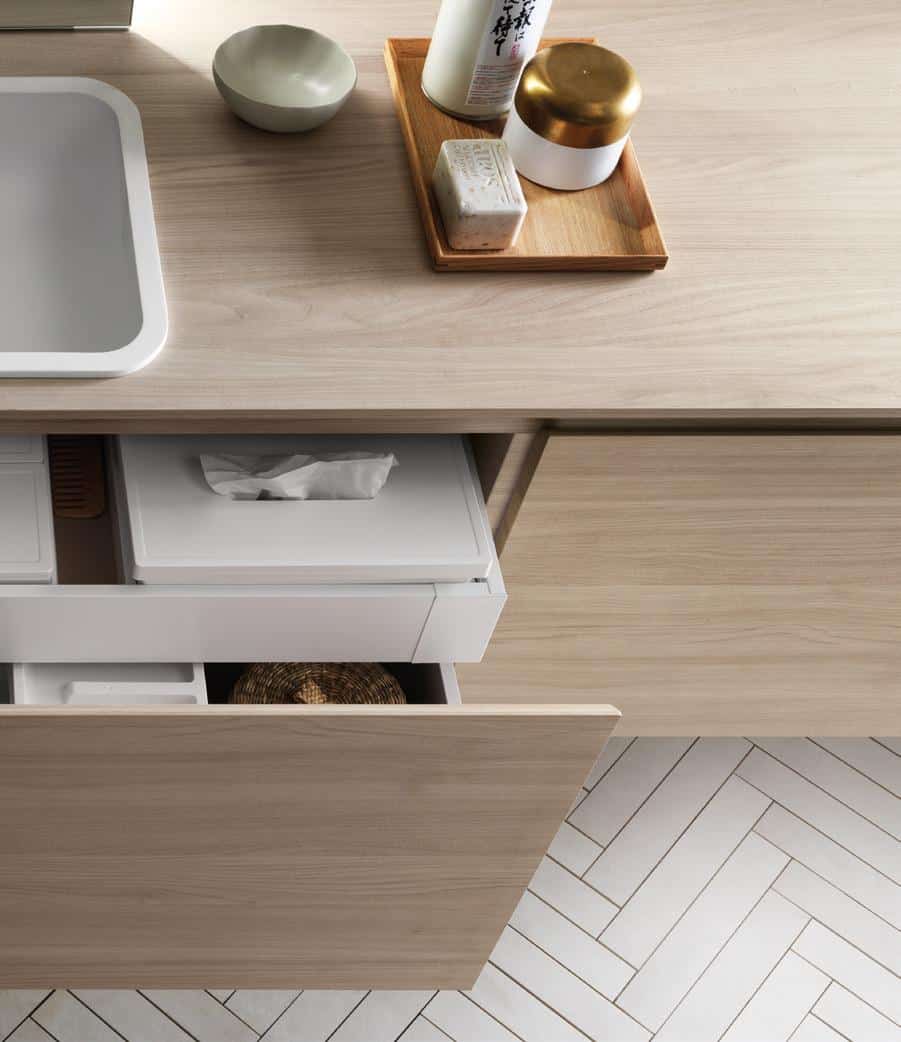Open wooden drawer in a kitchen with organized storage containers, a countertop with trays, bottles, a bowl, and a visible tile floor pattern.
