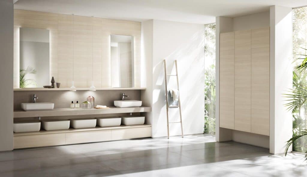 Modern bathroom with two rectangular sinks, large mirrors, and minimalist wooden cabinetry. A ladder with towels is placed against the wall, and the room is surrounded by glass walls allowing natural light and views of greenery.