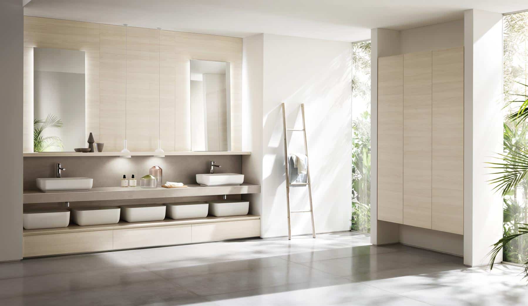 Modern bathroom with two rectangular sinks, large mirrors, and minimalist wooden cabinetry. A ladder with towels is placed against the wall, and the room is surrounded by glass walls allowing natural light and views of greenery.
