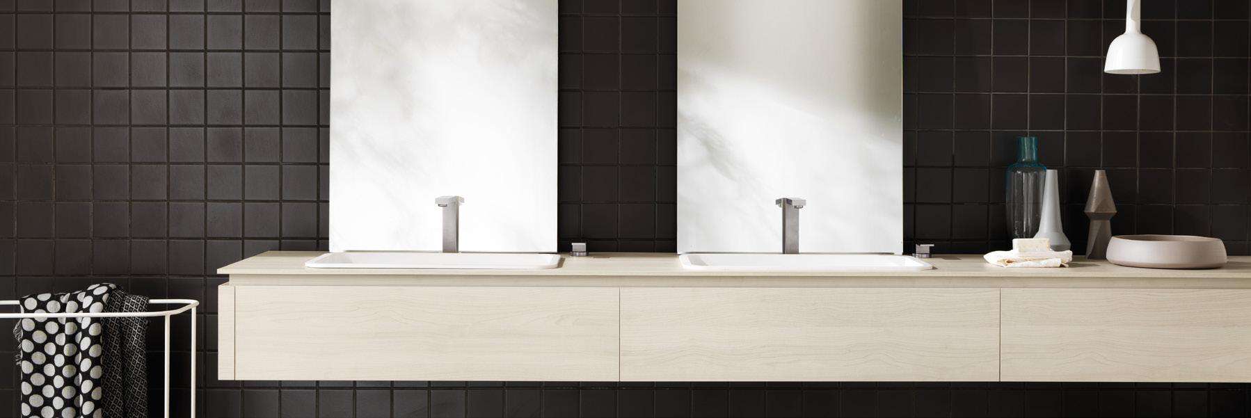 Modern bathroom with double sinks, square mirrors, and dark tiled wall.