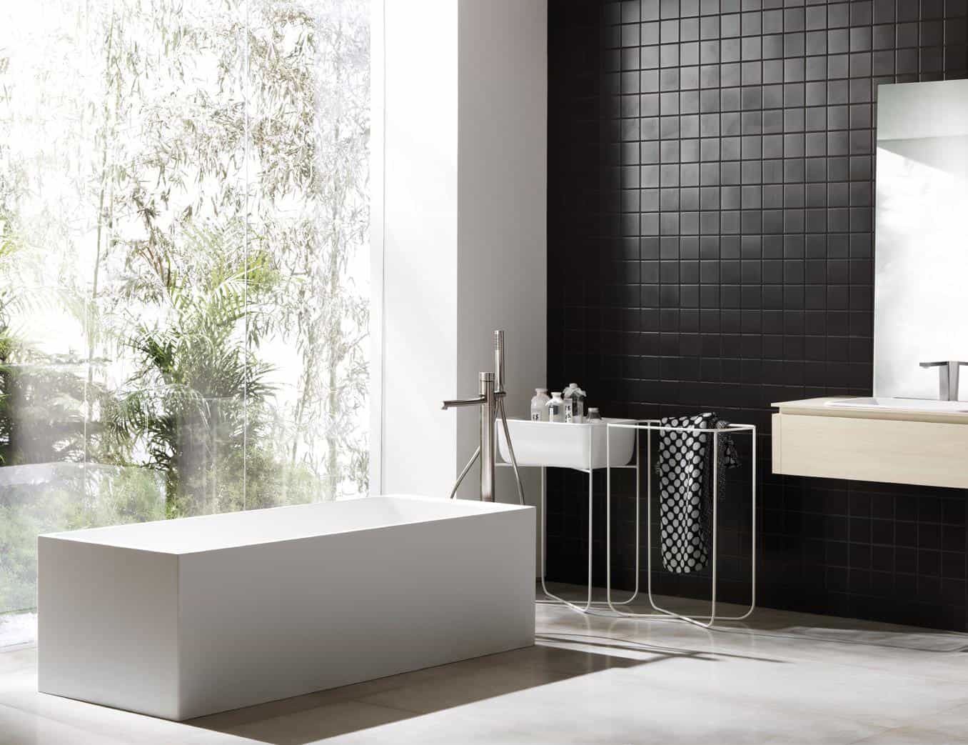 Modern bathroom with a rectangular white tub, black tiled wall, light wood vanity, large window, and a view of greenery.