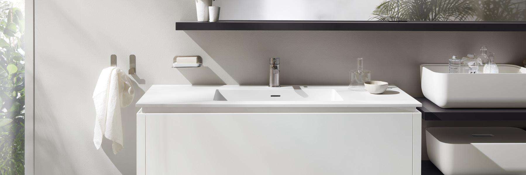 Modern bathroom sink with a sleek faucet, a towel on a hook, and a soap dish mounted on a light-colored wall.