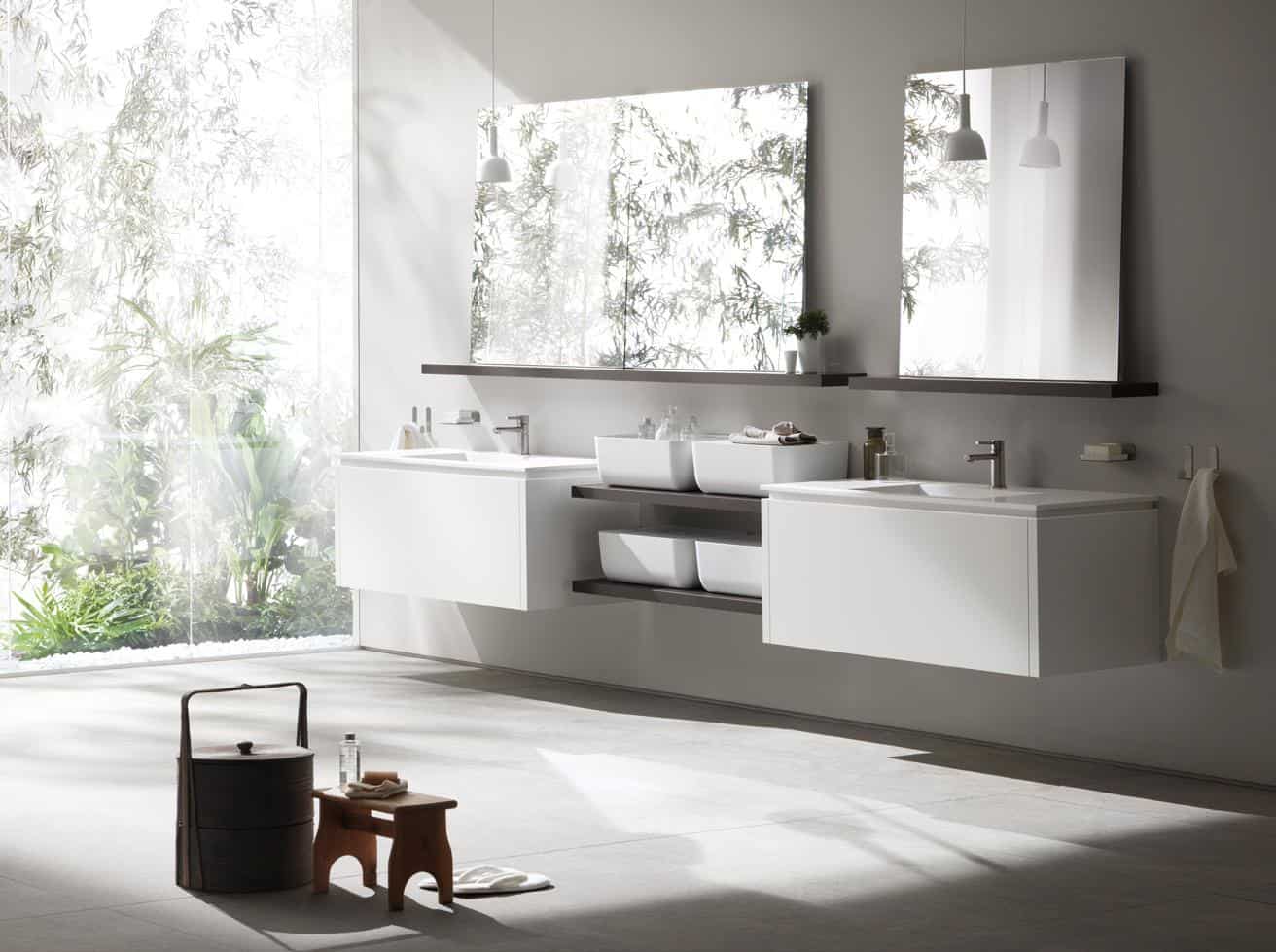Modern bathroom with floating vanities, rectangular mirrors, and natural light from a large window overlooking greenery.