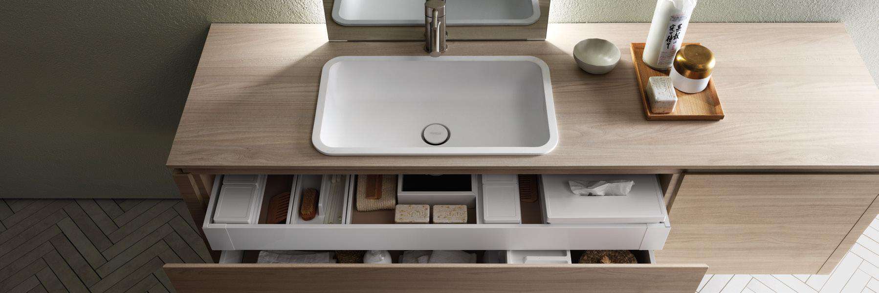 Modern bathroom vanity with a white sink, storage drawers, and toiletries on the countertop.