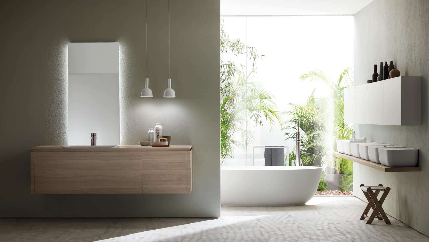 Modern bathroom with a minimalist design, featuring a wooden vanity, illuminated mirror, white freestanding bathtub, pendant lights, and abundant greenery.