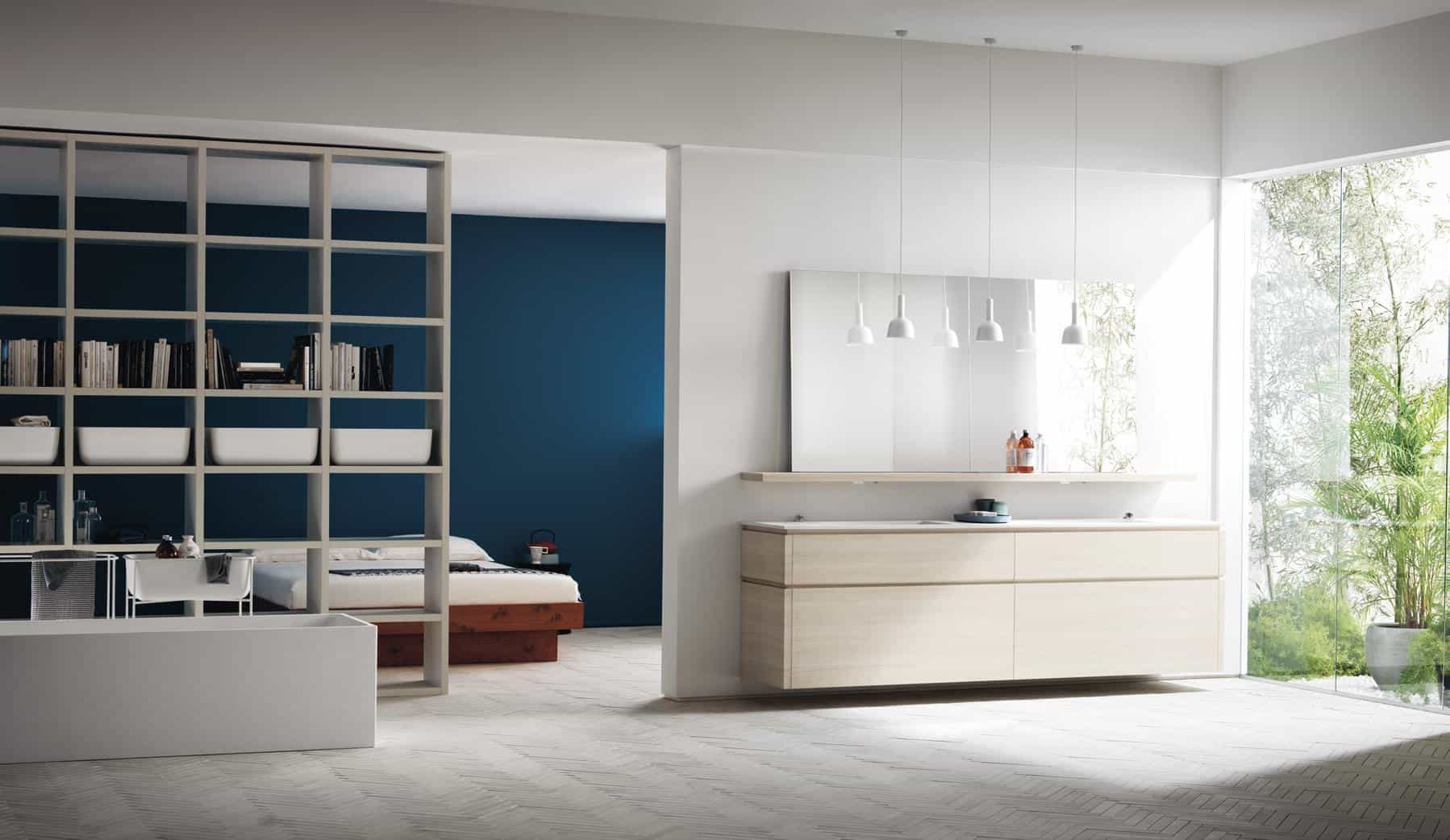 Modern open-concept interior with a living area, bookshelf partition, and minimalistic decor; large glass windows overlook greenery.