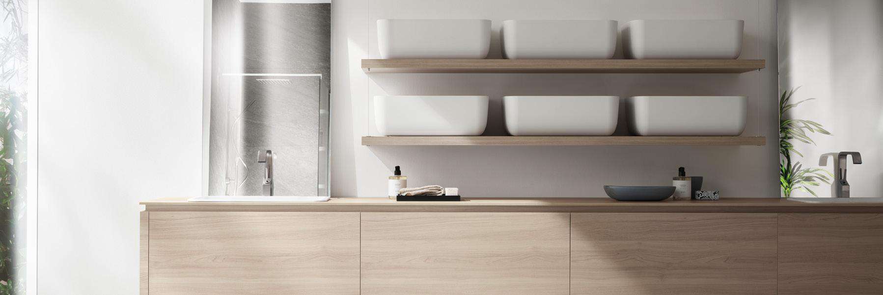 A modern kitchen with light wood cabinetry, a white countertop, double faucets, shelves with bowls, and a window view.