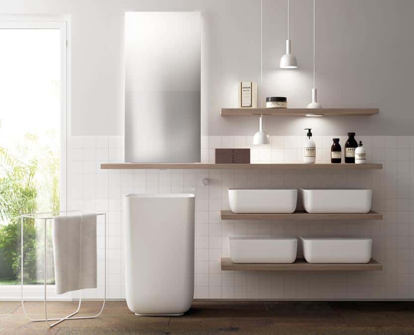 Minimalist bathroom with a tall white pedestal sink, wooden shelves holding toiletries, square white tiles, and pendant lights.