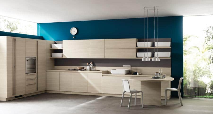 Modern kitchen with light wood cabinets, blue accent wall, built-in appliances, and a round table with chairs.
