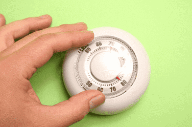 Hand adjusting a round, analog thermostat against a green background.
