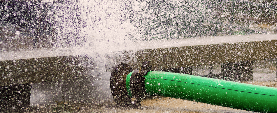 Green pipe gushing water forcefully onto the ground, creating splashes and spray in multiple directions.