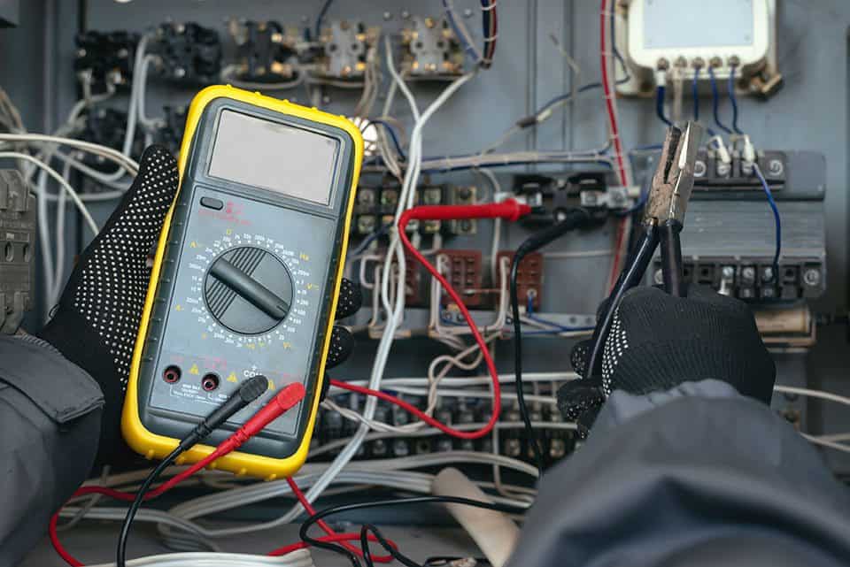 Person using a multimeter and pliers to test electrical connections in a panel.