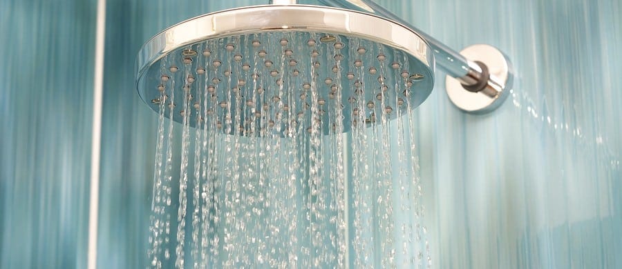 Close-up of a silver showerhead with water streaming down, set against a blue-tiled bathroom wall.