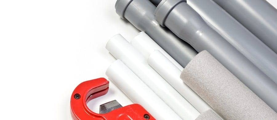 A selection of grey and white PVC pipes, a foam pipe insulator, and a red pipe cutter are arranged on a white surface.