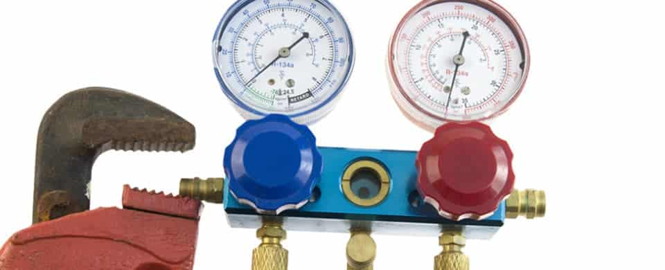 A pipe wrench and a blue manifold gauge with red and blue dials are arranged against a white background.