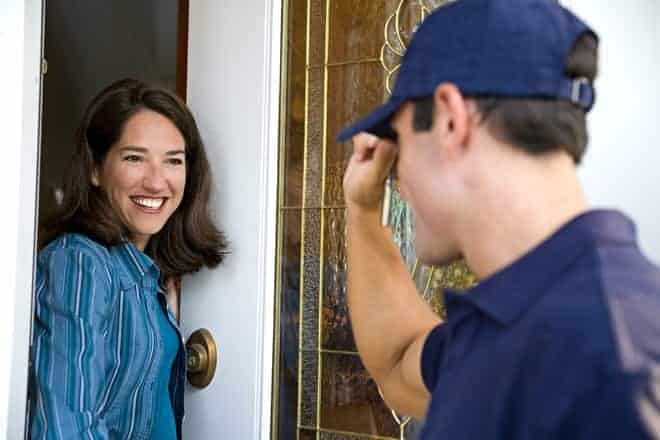 A woman is smiling at a person wearing a cap at her door. The person appears to be a delivery worker or visitor.