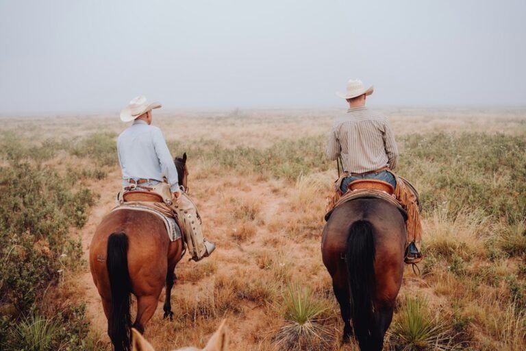 Two cowboys on horseback riding across the West Texas plains.