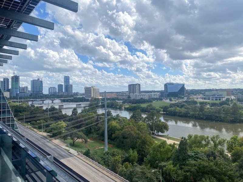 A view of the Austin skyline with blue sky, clouds, and green trees alongside the lake.
