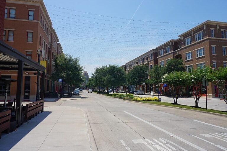 A glimpse of downtown Frisco with large buildings and blooming trees.