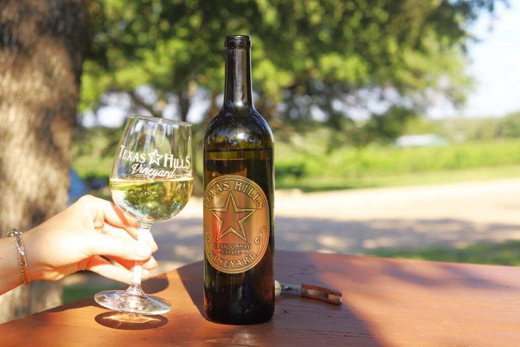 A bottle of Texas Hills Vineyard next to a hand holding a glass.