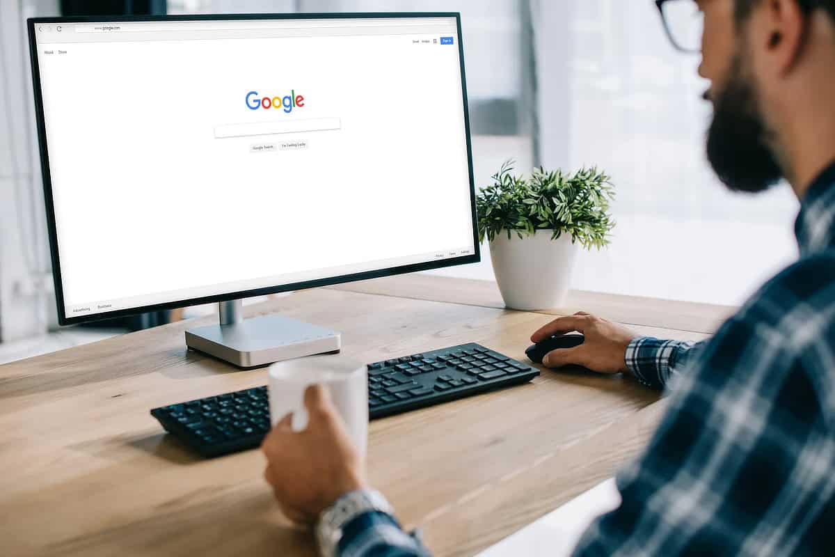 A man in a blue plaid shirt, out of focus, looking at a computer monitor with Google on the screen.