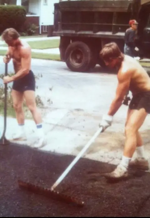 Two workers from Legacy Paving are laying fresh asphalt on a driveway, showing a team working hard to improve the property.