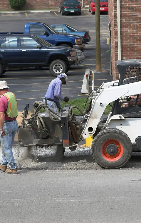 Two workers from Legacy Paving safely repair pavement using machines, showing their teamwork and skill in commercial paving services.