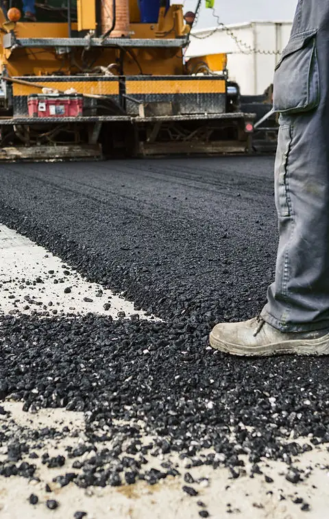 A Legacy Paving worker uses a machine to make a new, smooth road, showing careful work and fresh asphalt.