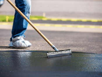A worker from Legacy Paving carefully adds sealant to a driveway, showing attention and skill in asphalt repair.