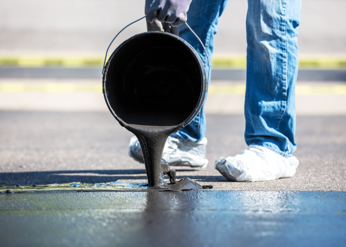 A worker adds black sealant to pavement, showing Legacy Paving cares for safe and well-maintained driveways.