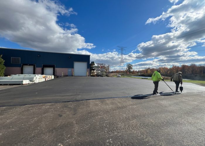 Two workers from Legacy Paving walk across a smooth, freshly paved lot, showing the company’s reliable commercial paving work.
