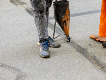 Someone from Legacy Paving carefully repairs a crack in an asphalt surface, showing the skill needed for professional paving work.