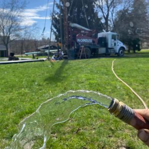 A McCandless Well Drilling truck helps provide fresh, clean water to homes, shown by water pouring from a hose onto grass.