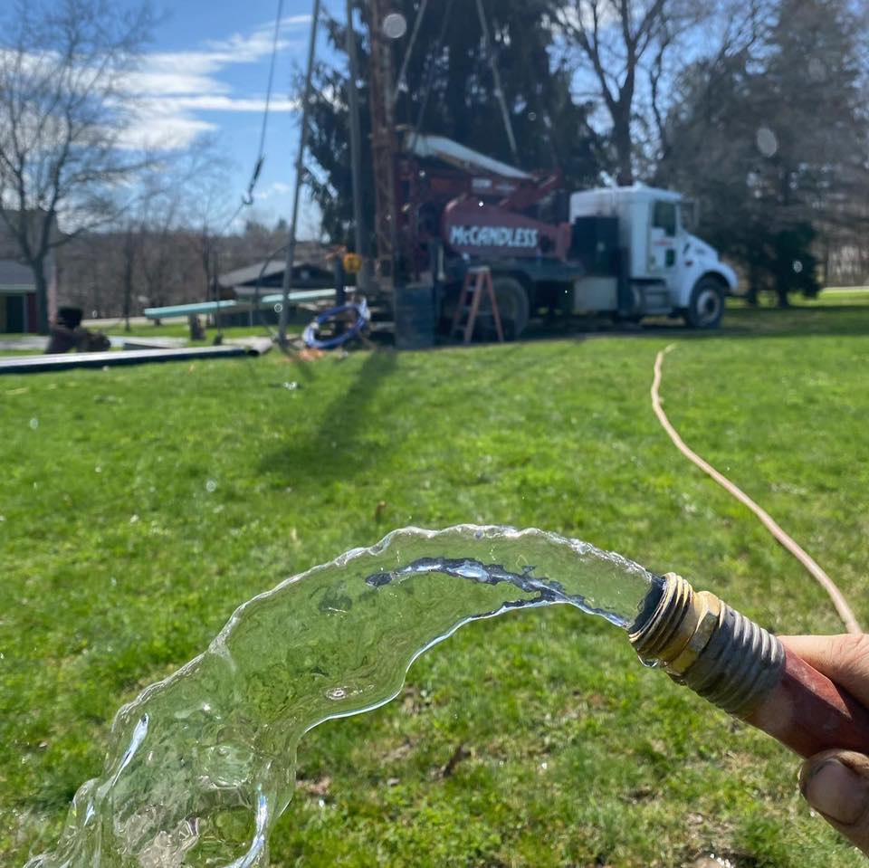 A McCandless Well Drilling truck helps provide fresh, clean water to homes, shown by water pouring from a hose onto grass.