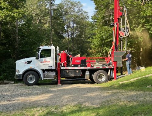 A McCandless Well Drilling truck is ready for water well service, showing a worker preparing to drill near the woods.