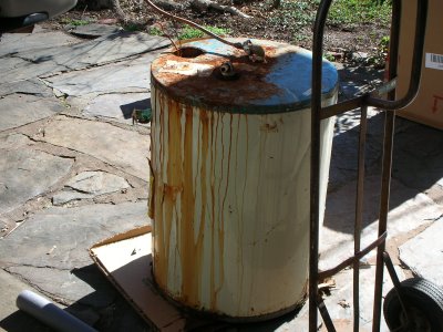 Rusty old water heater on a stone patio, next to a hand truck.