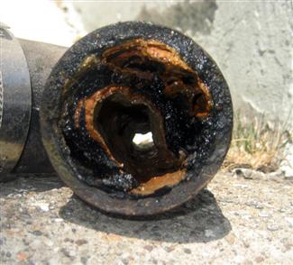 Cross-section of a corroded and clogged pipe with layers of rust and debris accumulation.