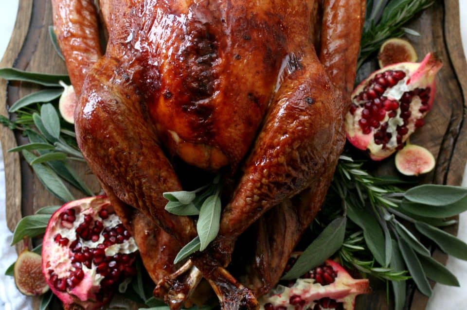 Roast turkey garnished with pomegranate halves, figs, and fresh herbs on a wooden platter.