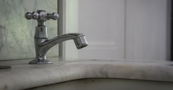 Close-up of a vintage metal faucet with cross handles on a marble countertop in a dimly lit bathroom.