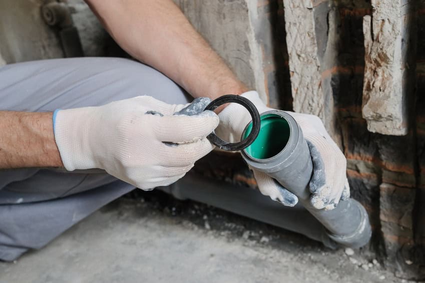 Person wearing gloves fixing a green pipe with a black rubber seal in a construction setting.