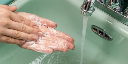 Hands with soap lather being washed under running water in a green sink.