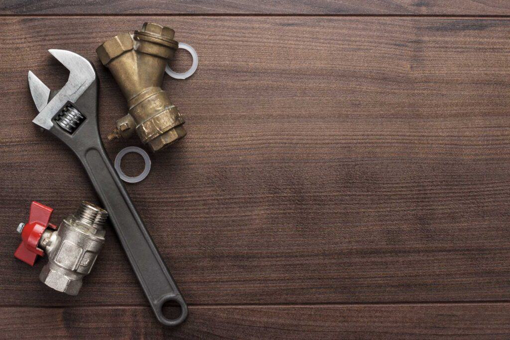 An adjustable wrench and brass plumbing fittings with washers are placed on a wooden surface.